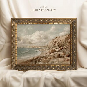 May include: An antique-style framed landscape painting of a coastal scene. The artwork depicts a beach with a rocky cliffside, ocean waves, and a cloudy sky. The frame is ornate with a gold finish. The text "VENUS NISH ART GALLERY" is at the top.