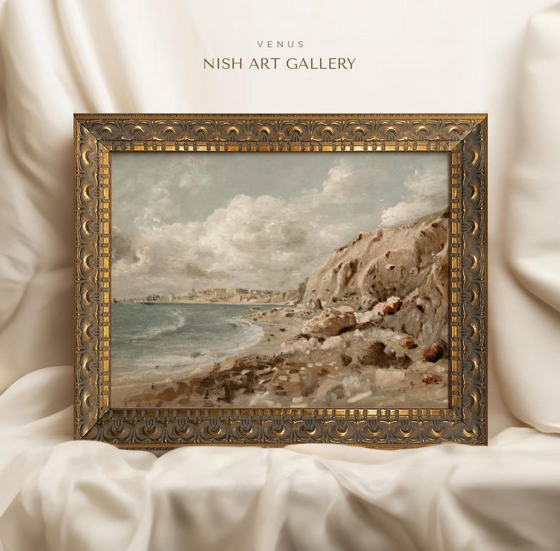 May include: An antique-style framed landscape painting of a coastal scene. The artwork depicts a beach with a rocky cliffside, ocean waves, and a cloudy sky. The frame is ornate with a gold finish. The text "VENUS NISH ART GALLERY" is at the top.