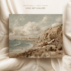 May include: An unframed print of a coastal landscape painting. The artwork depicts a beach with a rocky cliffside and a town in the distance. The sky is filled with fluffy clouds. The text "UNFRAMED / ONLY PRINT" and "NISH ART GALLERY" is visible.