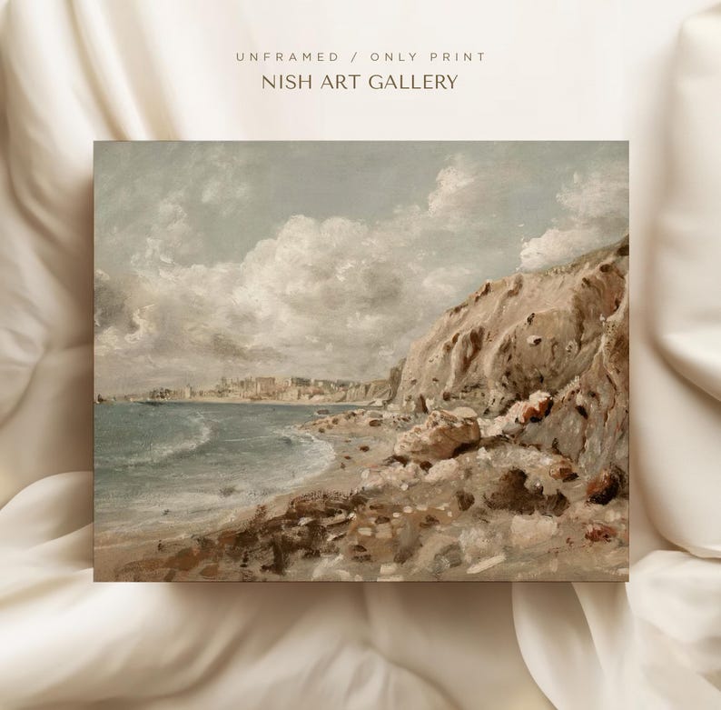 May include: An unframed print of a coastal landscape painting. The artwork depicts a beach with a rocky cliffside and a town in the distance. The sky is filled with fluffy clouds. The text "UNFRAMED / ONLY PRINT" and "NISH ART GALLERY" is visible.
