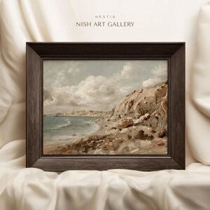 May include: A framed landscape painting of a coastal scene with a rocky cliff, beach, and ocean under a cloudy sky. The painting is in a dark brown wooden frame. The text "HESTIA NISH ART GALLERY" is at the top.
