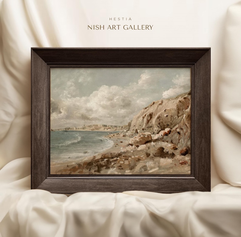May include: A framed landscape painting of a coastal scene with a rocky cliff, beach, and ocean under a cloudy sky. The painting is in a dark brown wooden frame. The text "HESTIA NISH ART GALLERY" is at the top.