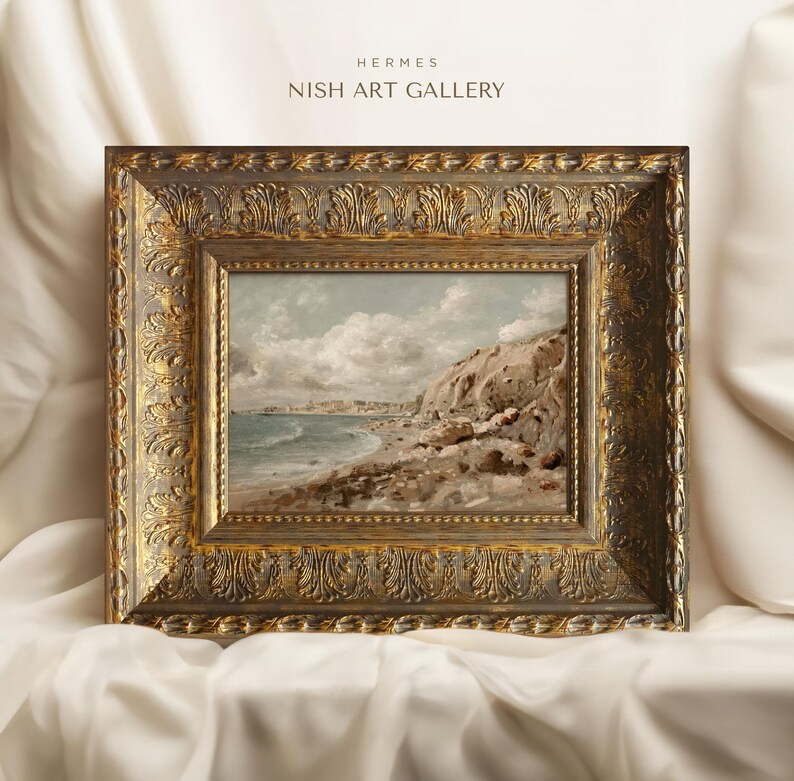 May include: A framed landscape painting of a coastal scene with a rocky cliff, beach, and ocean under a cloudy sky. The ornate gold frame features detailed carvings. The text "HERMES NISH ART GALLERY" is at the top.