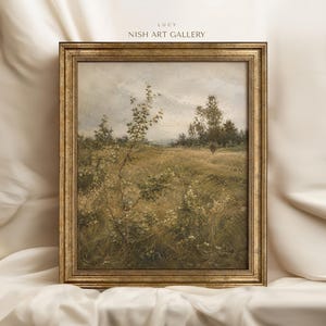 Op de afbeelding: Een ingelijst landschapsschilderij in een versierde goudkleurige lijst met een veld vol hoog gras, wilde bloemen en verspreide bomen onder een bewolkte lucht. De tekst LUCY NISH ART GALLERY staat in kleine zwarte letters boven de lijst.