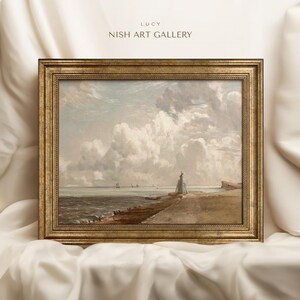 May include: A framed painting depicting a seascape with a lighthouse on a rocky shore. The sky is filled with fluffy white clouds, and the sea is a calm blue. The painting is in a gold frame.