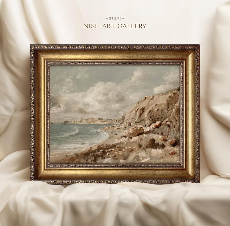 May include: A framed landscape painting of a coastal scene. The artwork features a beach with waves, cliffs, and a town in the distance. The frame is ornate with a gold finish. The text "ASTERIA NISH ART GALLERY" is at the top.