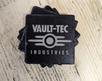 Może przedstawiać: Stos czarnych łupkowych podkładek z białym logo Vault-Tec Industries. Kwadratowe podkładki mają nieregularne krawędzie i spoczywają na jasnej drewnianej powierzchni. Logo zawiera okrąg z poziomymi liniami i napis "VAULT-TEC INDUSTRIES".