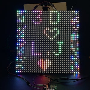 May include: A close-up of a colorful LED display panel with a grid of lights. The panel is displaying a pattern of different colored lights, including red, green, blue, and white.