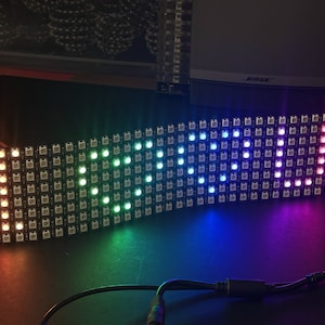 Op de afbeelding: Een gebogen LED-matrix die een regenboog aan kleuren weergeeft. De lampjes zijn in een raster gerangschikt, waarbij elke LED een andere tint uitstraalt. De kleuren gaan soepel over in elkaar, waardoor een levendig visueel effect ontstaat.