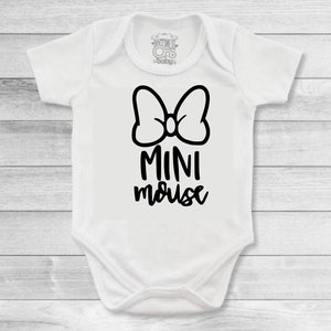 Op de afbeelding: Witte baby romper met een zwarte strik en de tekst "MINI mouse" gedrukt op de voorkant.