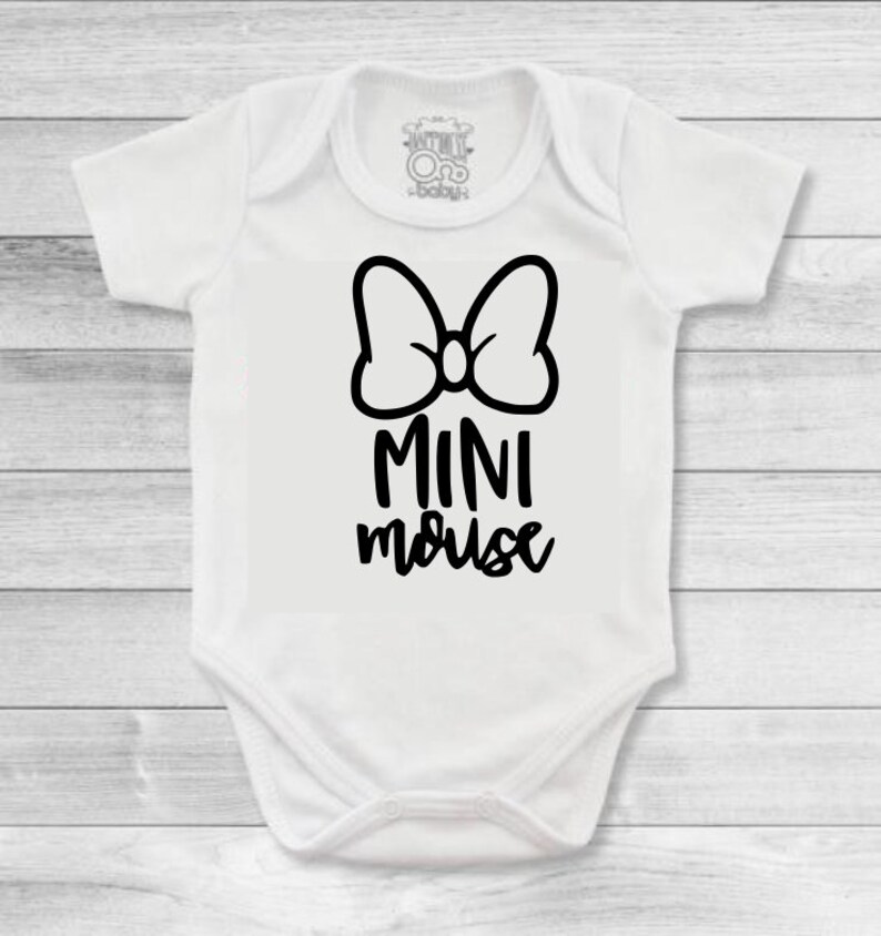 Op de afbeelding: Witte baby romper met een zwarte strik en de tekst "MINI mouse" gedrukt op de voorkant.