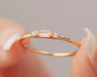 May include: A delicate gold ring with a rectangular clear gemstone and two smaller round clear gemstones on either side.