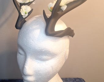 May include: A dark brown antler headband with white floral accents. The antlers are attached to a white foam head. The headband is a unique accessory for themed events or costumes.