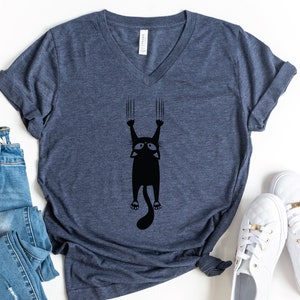 May include: A navy blue V-neck t-shirt with a black silhouette of a cat hanging from a surface with its claws extended.