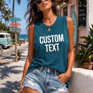 May include: Teal sleeveless vest top with the words "CUSTOM TEXT" in white block letters. The top is paired with denim shorts. The background includes a beach scene with palm trees and a sign that says "BEACH SURF CAFE".