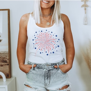 Puede incluir: Camiseta blanca de tirantes con un gr&aacute;fico de fuegos artificiales rojo, blanco y azul. El gr&aacute;fico est&aacute; rodeado de estrellas azules.