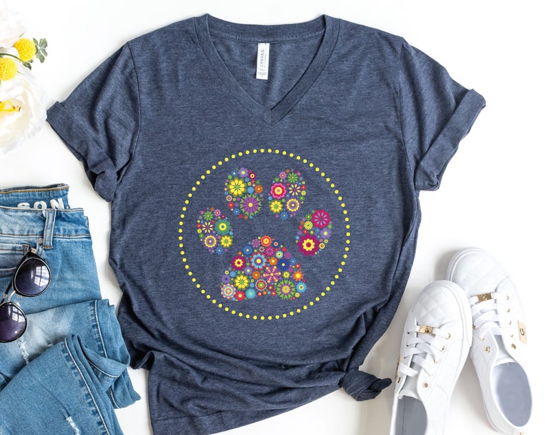 May include: A navy blue t-shirt featuring a floral paw print design. The paw print is encircled by a yellow circle with yellow dots.