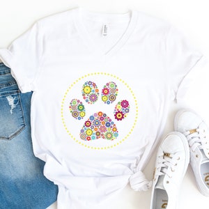 May include: White t-shirt featuring a colourful floral paw print design. The paw print is encircled by a yellow dotted circle.