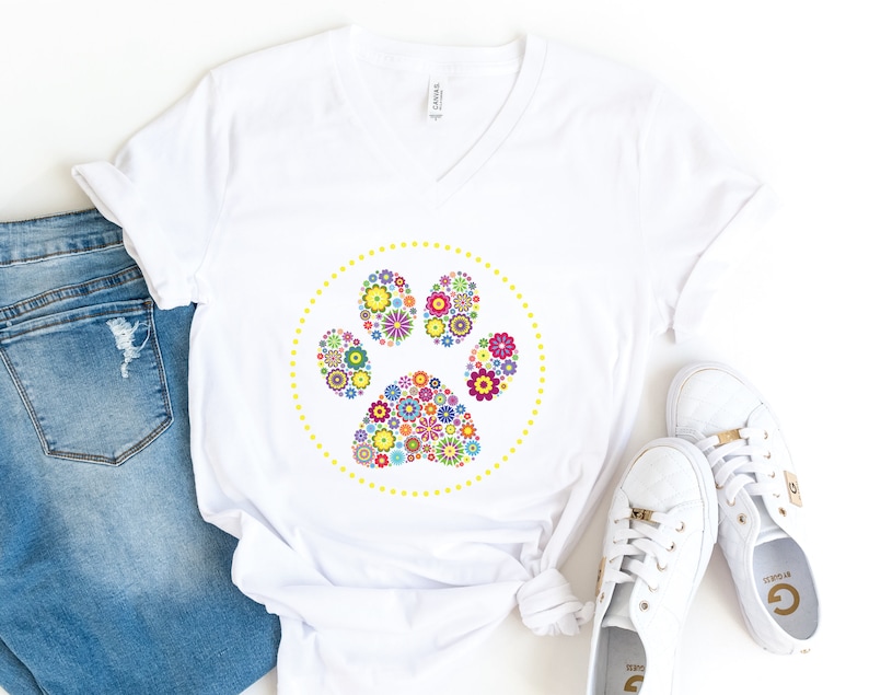 May include: White t-shirt featuring a colourful floral paw print design. The paw print is encircled by a yellow dotted circle.