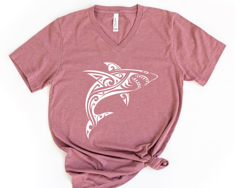 May include: A mauve v-neck t-shirt with a white tribal shark design.