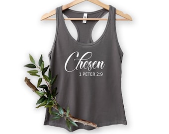 May include: A gray racerback tank top with the word "Chosen" in white script, and the text "1 Peter 2:9" below it. The tank top is hanging on a wooden hanger, with a decorative branch with green leaves.