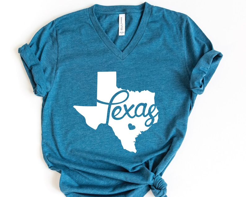 Puede incluir: Una camiseta azul turquesa con un contorno blanco del estado de Texas y la palabra "Texas" escrita en letra cursiva dentro del contorno.