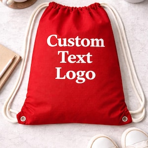 May include: A red drawstring bag with the words "Custom Text Logo" in white. The bag has white rope-like drawstrings and metal eyelets. A pair of white sneakers is visible in the bottom right corner.