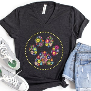 May include: A dark grey V-neck t-shirt with a floral paw print design. The paw print is surrounded by a yellow dotted circle.