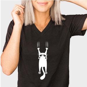 May include: Black v-neck t-shirt with a white graphic of a cat hanging upside down with its claws extended.
