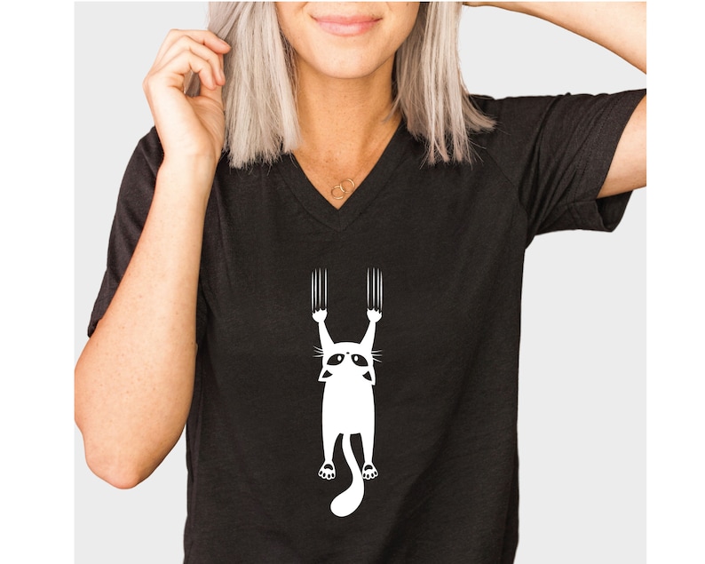 May include: Black v-neck t-shirt with a white graphic of a cat hanging upside down with its claws extended.