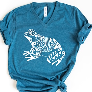 May include: A teal blue v-neck t-shirt with a white graphic of a stylized frog with intricate patterns.