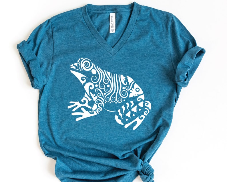 May include: A teal blue v-neck t-shirt with a white graphic of a stylized frog with intricate patterns.