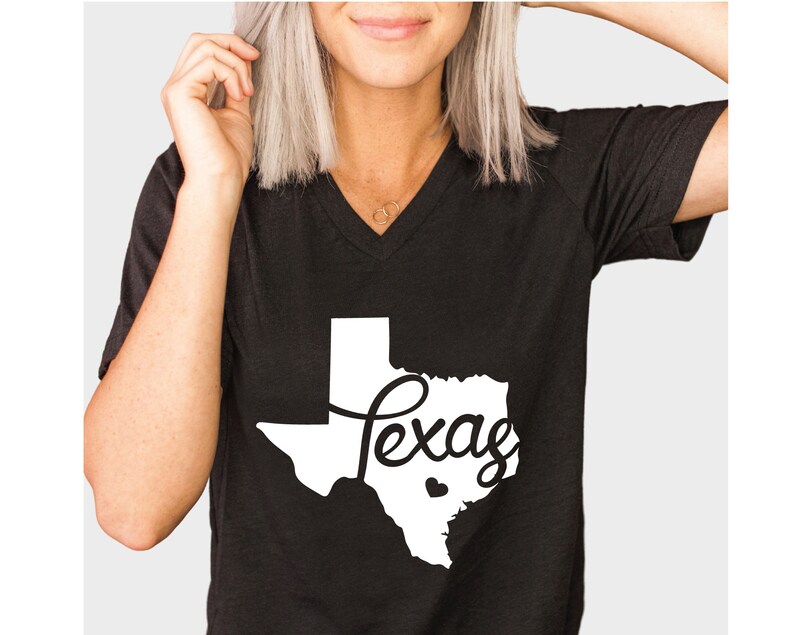Puede incluir: Camiseta negra de cuello en V con un contorno blanco del estado de Texas y la palabra "Texas" escrita en letra cursiva dentro del contorno. Un peque&ntilde;o coraz&oacute;n blanco est&aacute; dentro del contorno del estado.