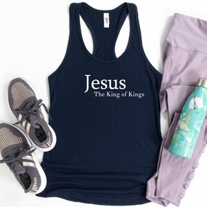 May include: Navy blue tank top with the text "Jesus The King of Kings" in white. The tank top is paired with gray athletic shoes, light purple leggings, and a teal water bottle with a floral design.