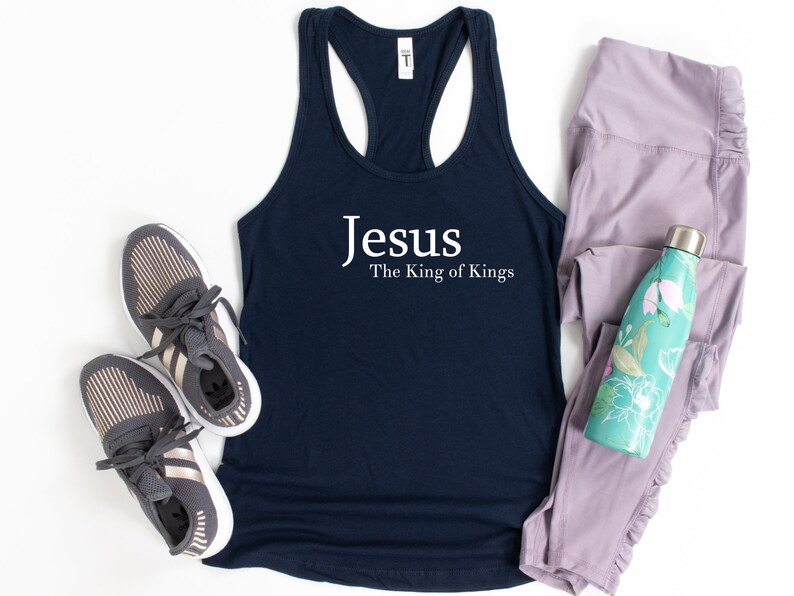 May include: Navy blue tank top with the text "Jesus The King of Kings" in white. The tank top is paired with gray athletic shoes, light purple leggings, and a teal water bottle with a floral design.