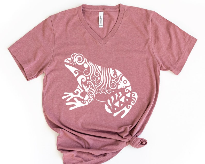 May include: A mauve v-neck t-shirt with a white stylized frog design.