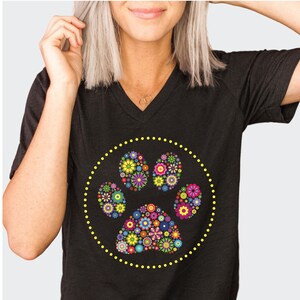 May include: Black V-neck t-shirt with a yellow circle design featuring a colourful floral paw print.
