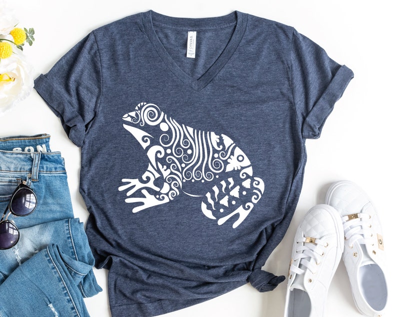 May include: A navy blue V-neck t-shirt with a white stylized design of a frog. The frog is made up of intricate swirls and lines.
