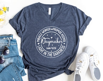 May include: A navy blue v-neck t-shirt with a white circle graphic that says "Waymaker" with the text "Miracle Worker, Promise Keeper, Light in the Darkness" around the circle. The text "Isaiah 43:16" is also included in the graphic.