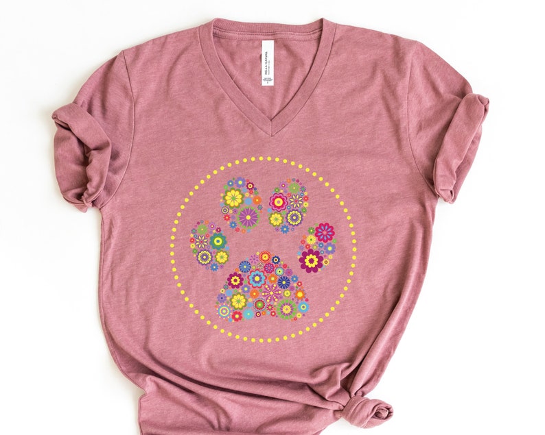 May include: A mauve v-neck t-shirt featuring a floral paw print design. The paw print is made up of colourful flowers and is surrounded by a circle of yellow dots.