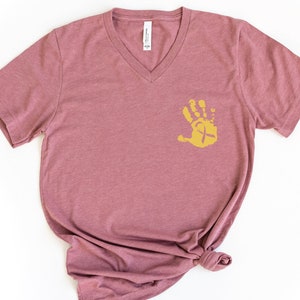 May include: A mauve v-neck t-shirt with a gold handprint design featuring a yellow ribbon. The handprint is on the left side of the shirt.