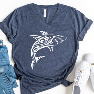 May include: A navy blue t-shirt with a white tribal shark design. The shirt has a v-neck and short sleeves.