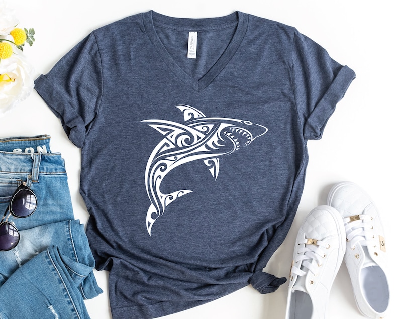 May include: A navy blue t-shirt with a white tribal shark design. The shirt has a v-neck and short sleeves.