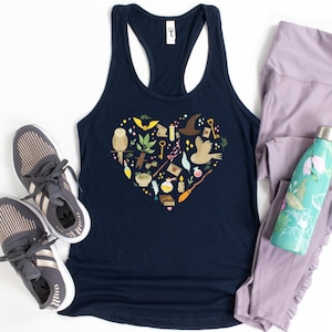 May include: Navy blue racerback tank top with a heart-shaped design filled with whimsical illustrations of an owl, keys, a broom, and a wizard's hat. Gray sneakers, lavender leggings, and a teal water bottle complete the ensemble.