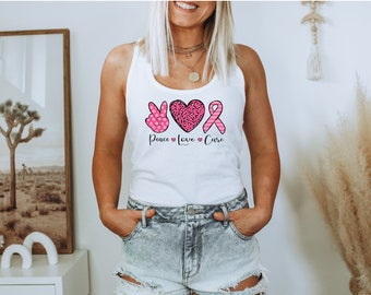 May include: White tank top with a pink peace sign, heart, and ribbon design. The text "Peace Love Cure" is printed below the design.
