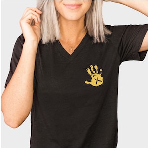 May include: Black v-neck t-shirt with a gold handprint design featuring a gold ribbon.