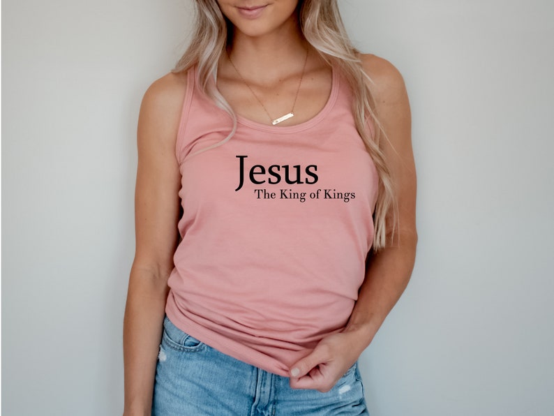 May include: A dusty rose tank top with the words "Jesus" above "The King of Kings" in black lettering. The top is a sleeveless style, made of a soft material.