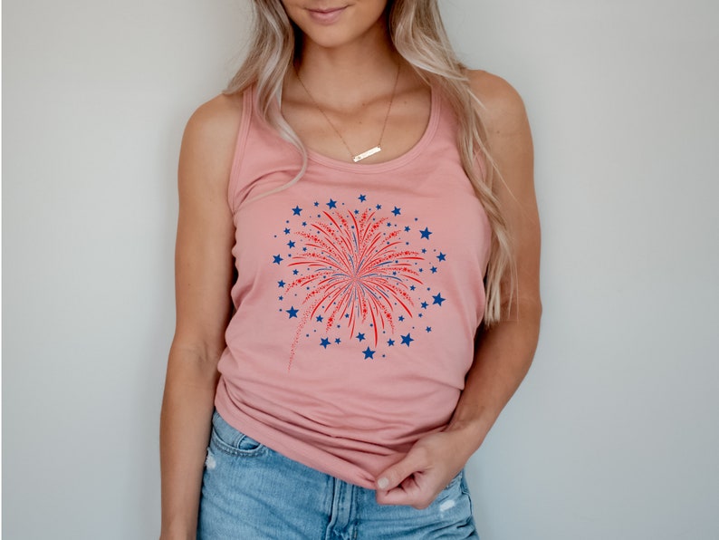 Puede incluir: Una camiseta de tirantes rosa con un gr&aacute;fico de fuegos artificiales rojo, blanco y azul. Los fuegos artificiales est&aacute;n rodeados de estrellas azules.