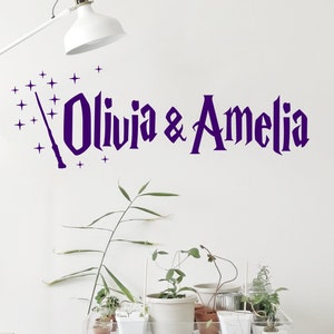 May include: Purple wall decal with the text "Olivia & Amelia" in a whimsical font, with a wand and stars above the names.