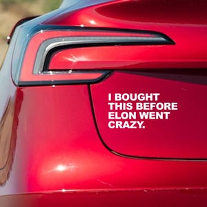 May include: A red car with a white sticker that says "I bought this before Elon went crazy."